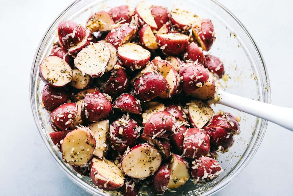 Chopped red potatoes being mixed with seasonings in a glass bowl.