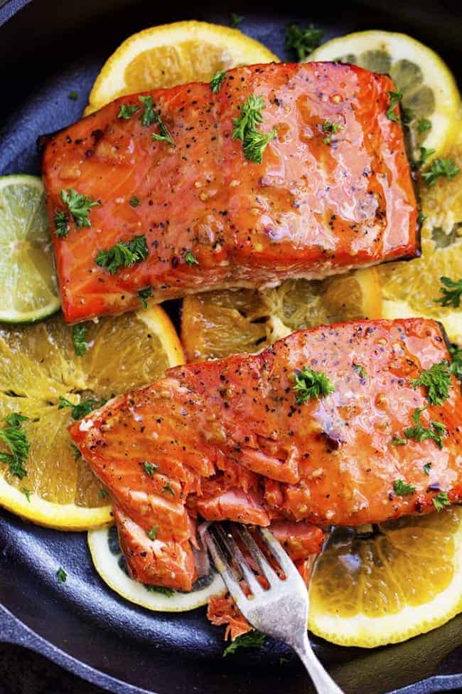 grilled citrus salmon on lemon slices in a skillet being cut into by a fork.