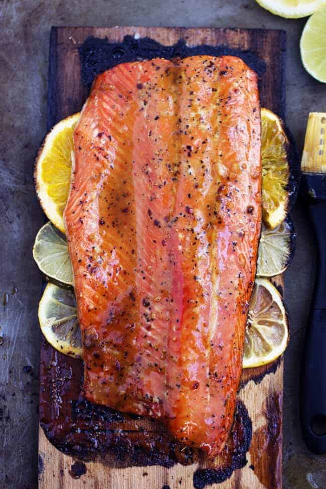 grilled triple citrus salmon on lemon slices on a wooden plank.