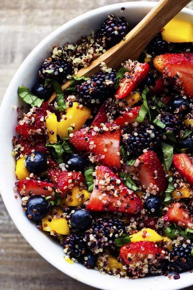 honey lime quinoa fruit salad in a white bowl with a wooden spoon.