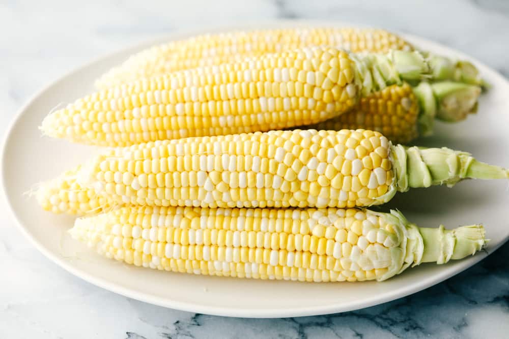 Fresh corn stacked on a white plate.