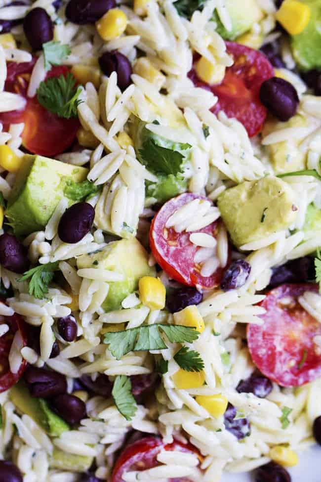 Close up on orzo pasta that is filled with corn, black beans, cilantro, avocado and cherry tomatoes.