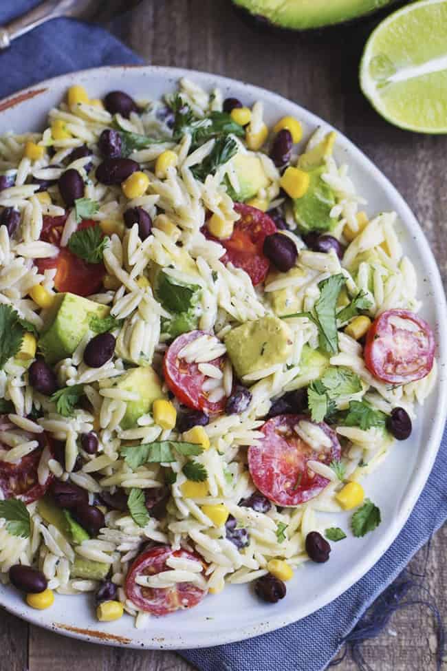 orzo pasta with corn, black beans, cilantro, avacado, and cherry tomatoes on a white plate.