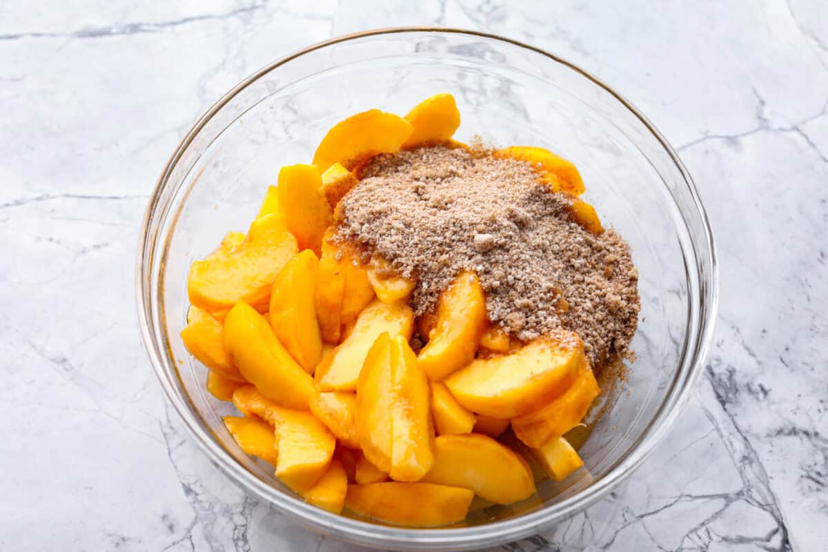 Overhead shot of fresh sliced peaches with cinnamon sugar mixture in glass bowl. 