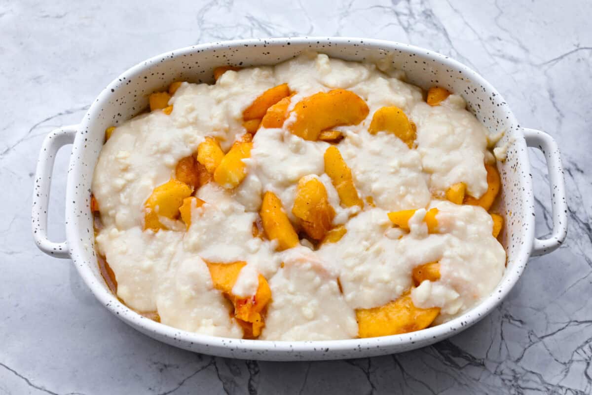 Overhead shot of old fashioned peach cobbler mixture topped with biscuit topping in baking dish, ready to be baked. 