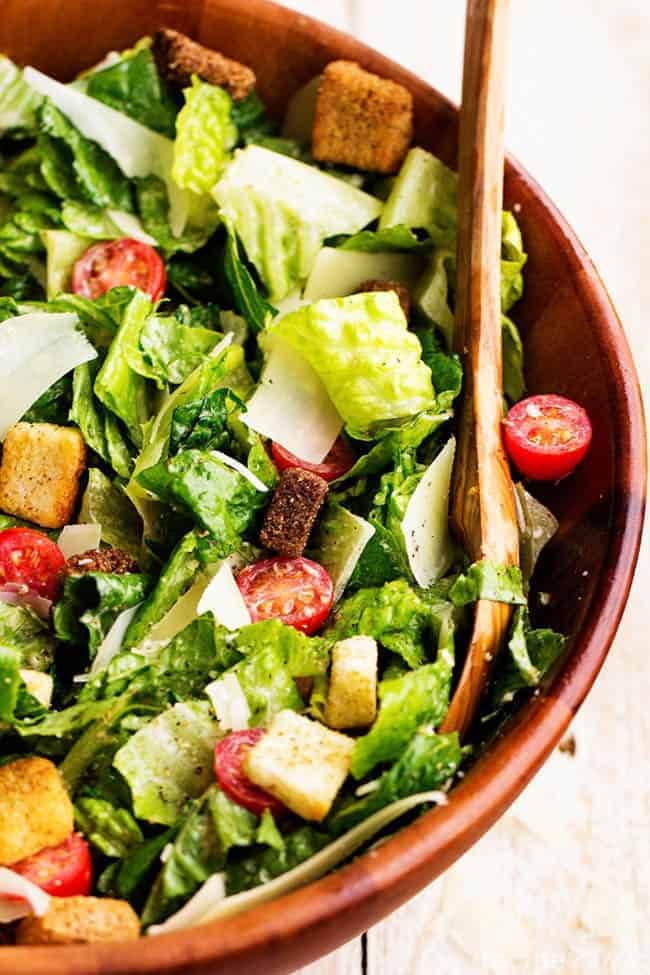 Klassischer Caesar-Salat in einer roten Schüssel mit Holzlöffel.