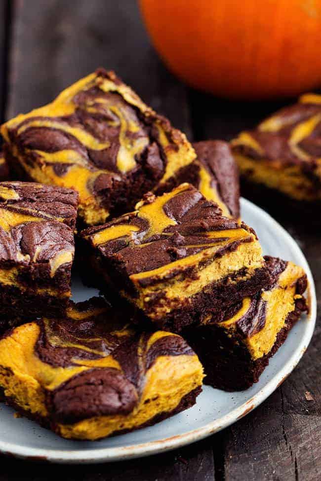 pumpkin cheesecake brownies stacked on a white plate.