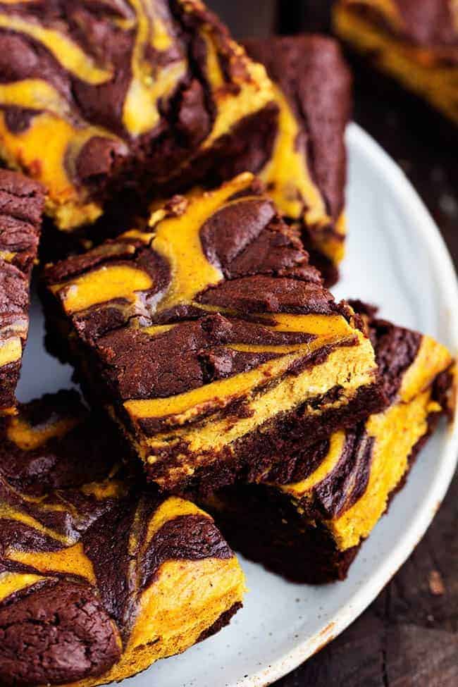 pumpkin cheesecake brownies stacked on a white plate.