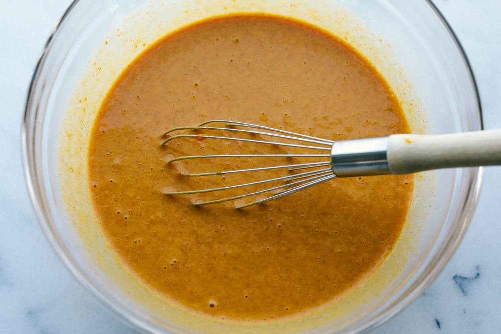 mixture of wet ingredients for the pumpkin pie in a glass bowl with a whisk