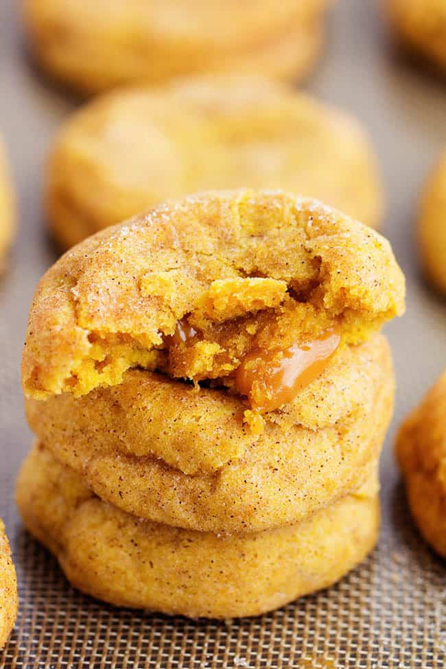 caramel pumpkin snickerdoodle cookies in a stack with the top cookie cut in half to show gooey inside.