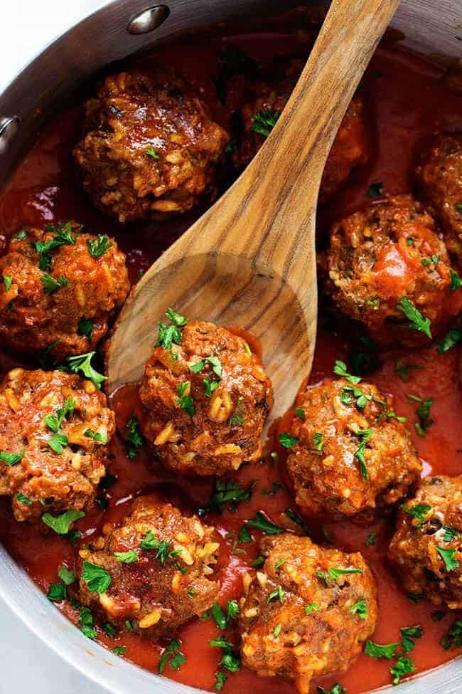 Porcupine Meatballs in a skillet cooking with a wooden spoon picking up a meatball. 