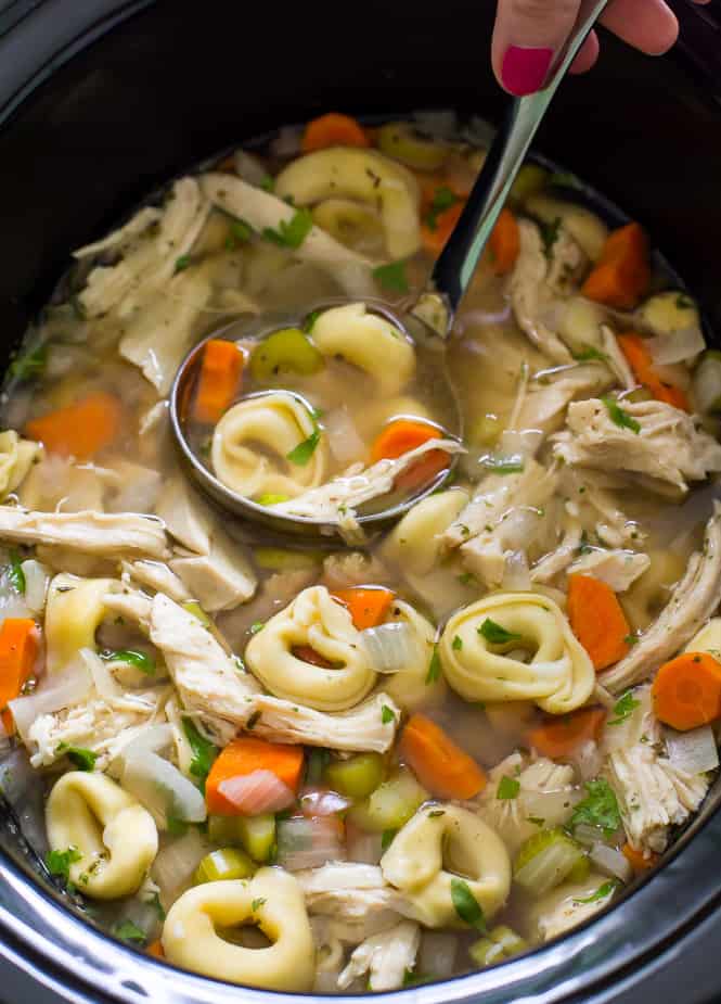 Slow cooker chicken tortellini soup in a slow cooker with a ladle 
