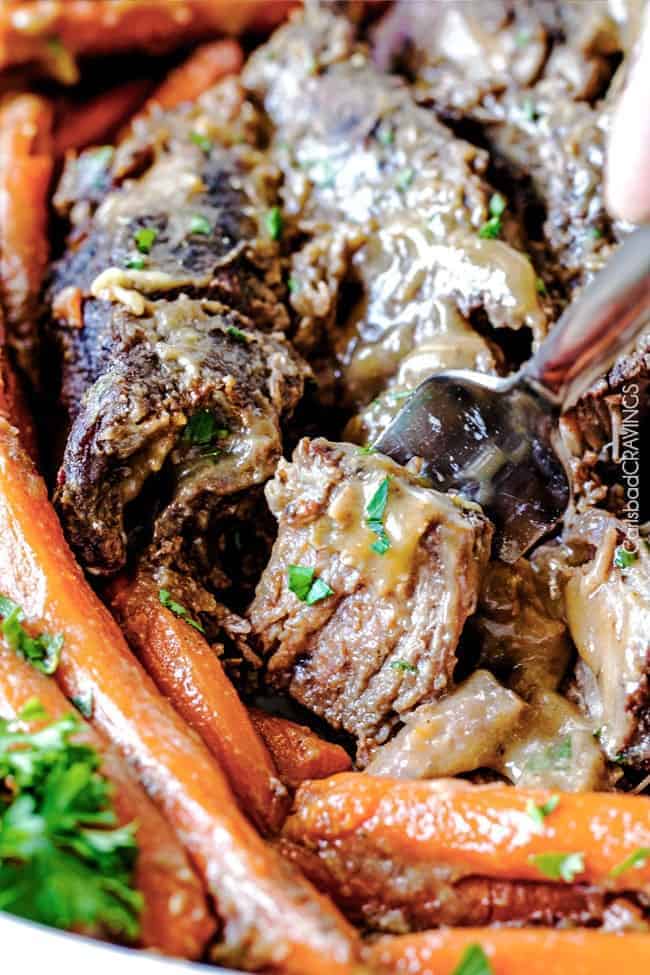 Pot roast close up with carrots and a fork pulling a bite of meat off.