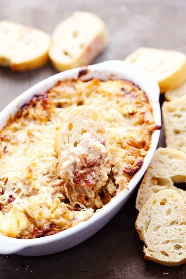 Hot Caramelized Onion and Bacon Dip in white dish with bread on side.