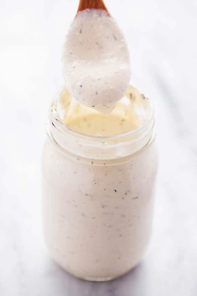 homemade Alfredo Sauce in a jar using a spoon to show how thick it is.