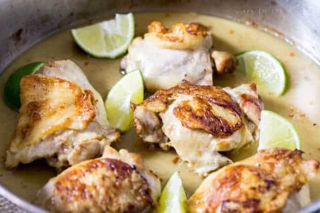 Chicken being seared in a frying pan with fresh cut limes on the side. 