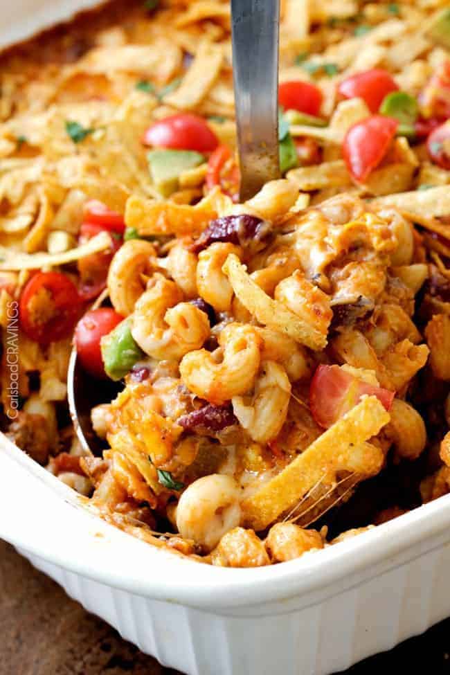 Taco chili pasta bake in a white casserole dish with a metal spoon removing some. 