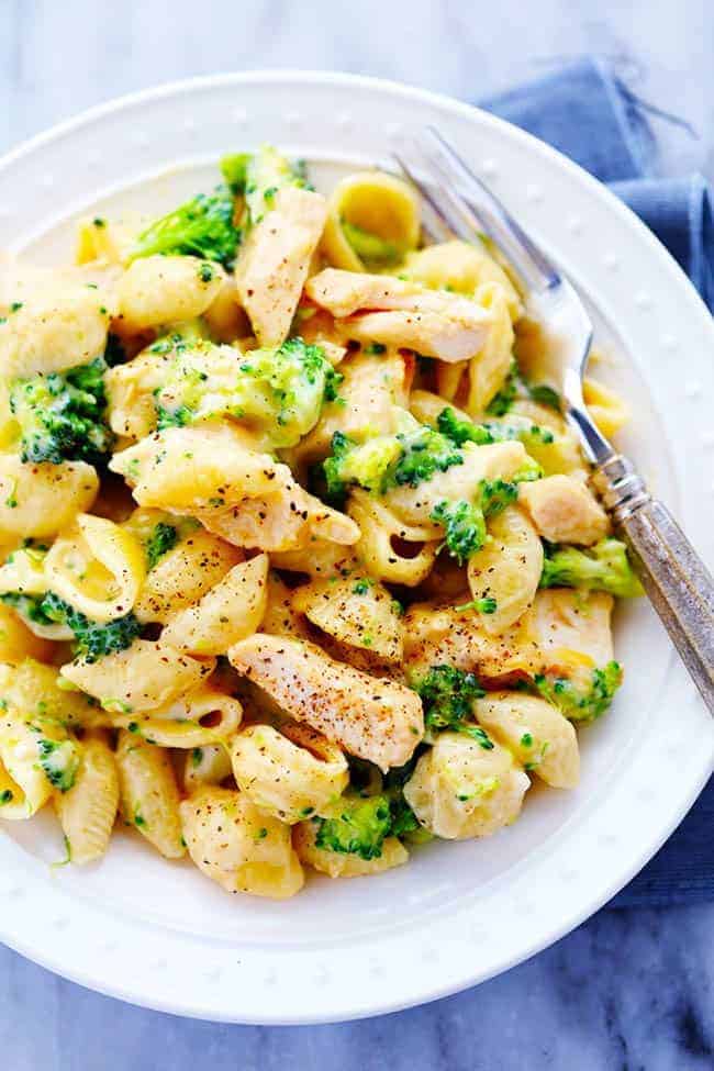 CHEESY CHICKEN BROCCOLI SHELLS ON A WHITE PLATE WITH A METAL FORK.  