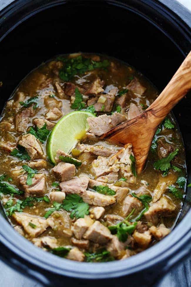 Slow cooker pork Chile Verde with a wooden spoon.