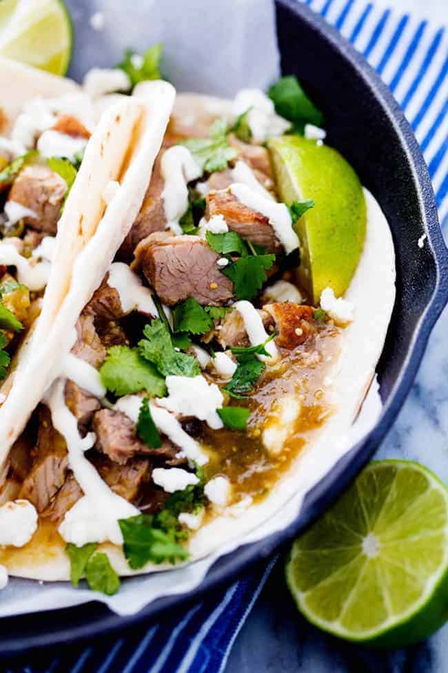 Slow Cooker Pork Chili Verde in pita tacos on a black plate with fresh cut limes on the side. 