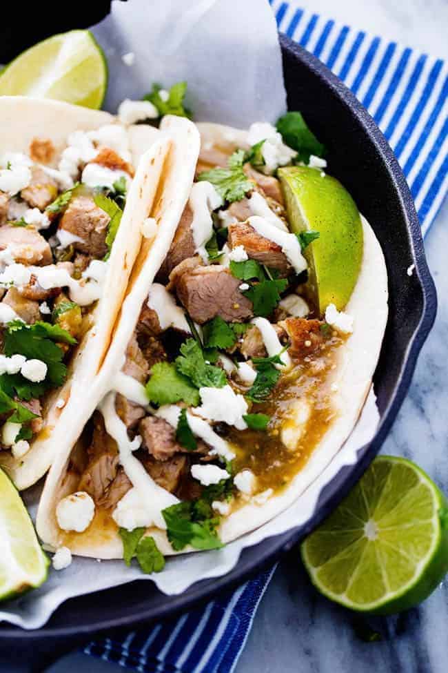 Slow Cooker Pork Chili Verde in pita tacos in a black plate with fresh limes on the side. 