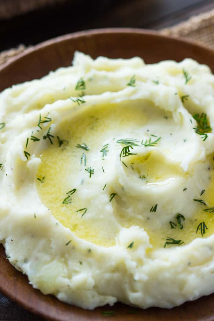 Close up photo of Slow Cooker Ranch Mashed Potatoes in a brown bowl. 