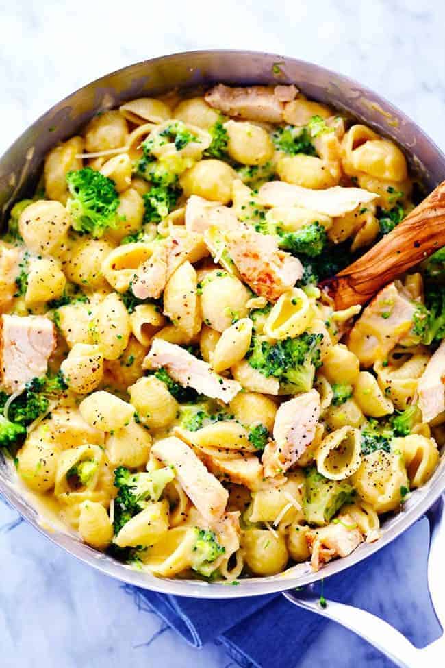 CHEESY CHICKEN BROCCOLI SHELLS IN A PAN WITH A WOODEN SPOON.  