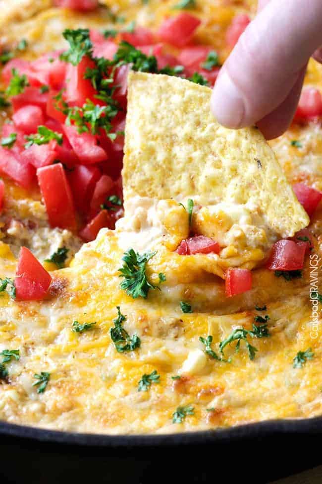 Queso verde corn dip with fresh sliced tomatoes on top with a chip being dipped into it. 