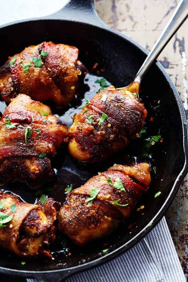 Sweet and spicy bacon wrapped chicken in a skillet with a spoon removing one.