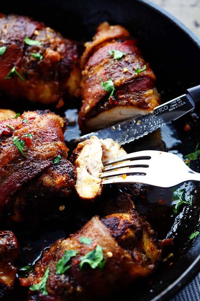 Sweetened spicy bacon wrapped chicken being sliced into with a fork and a knife in a skillet.