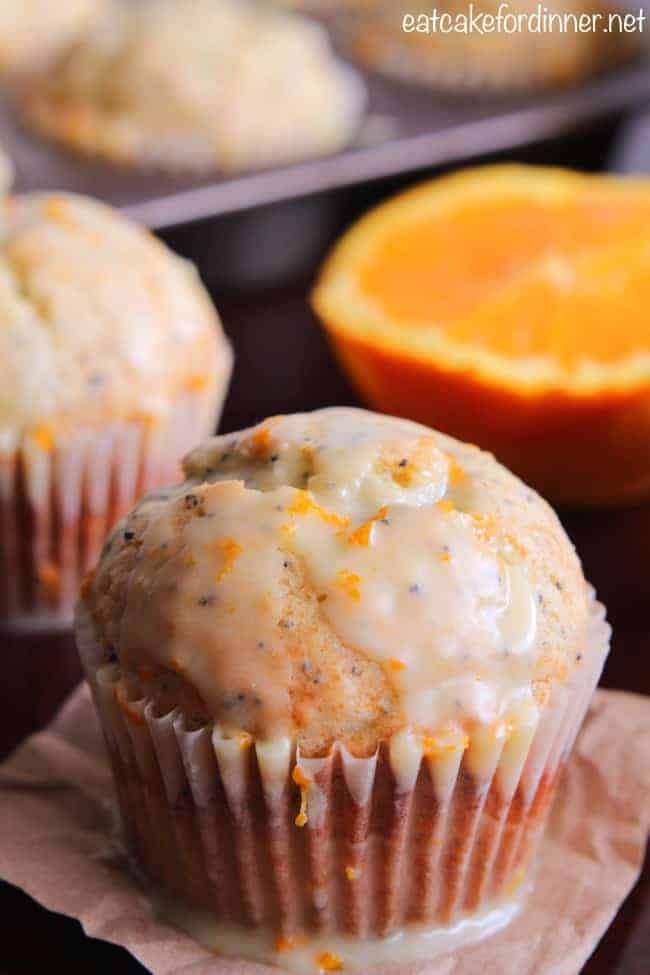 Banana Poppy Seed Muffins with an Orange Glaze and a fresh cut orange in the background. 