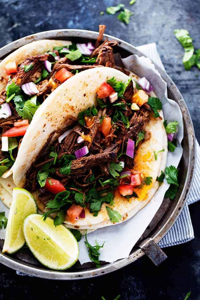 Barbacoa in a taco with tomatoes, onions and lettuce over top with limes on the side. 