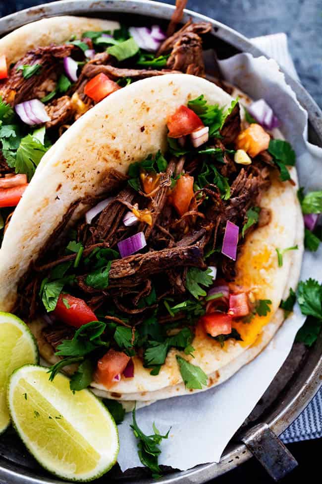 Beef barbacoa in a taco with tomatoes, onions and cilantro garnished with two limes on the side. 