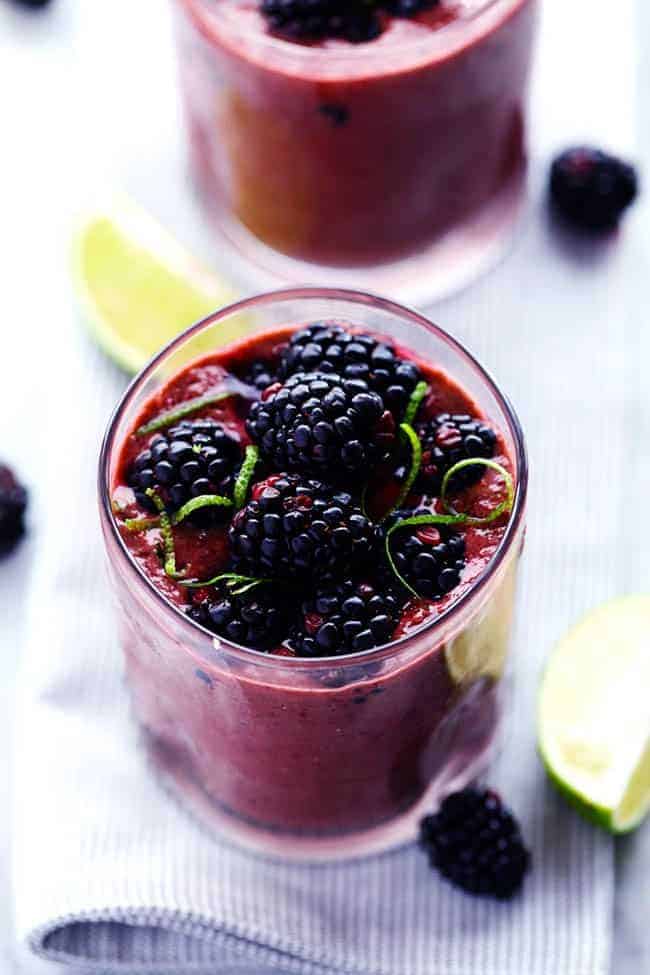 Up close photo of blackberry lime smoothie in a clear glass with fresh limes and blackberries on the side.