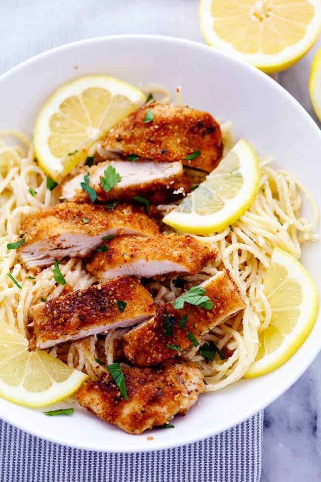 Crispy Parmesan Chicken with Creamy Lemon Garlic Pasta on a white plate with fresh sliced lemons on the side. 