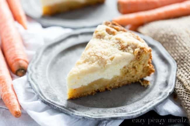 A slice of carrot coffee cake on a gray plate with fresh carrots on the side.