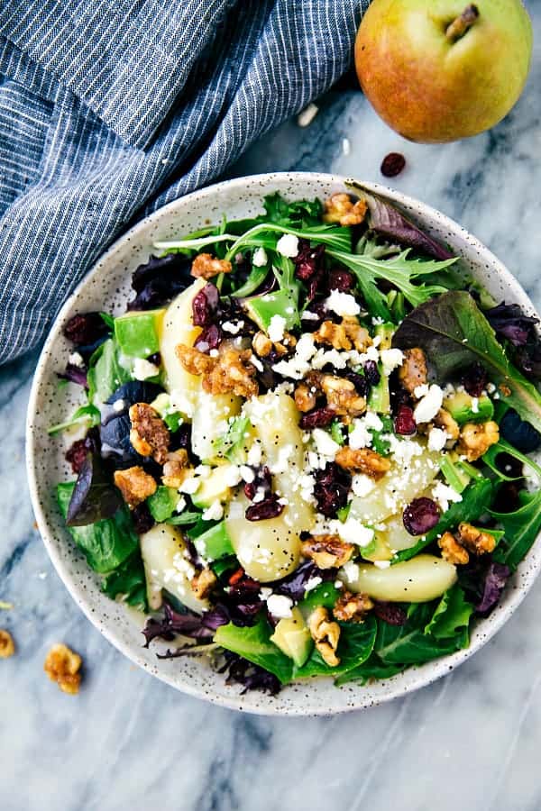 A bowl of salad topped with walnuts, apples and feta cheese. 