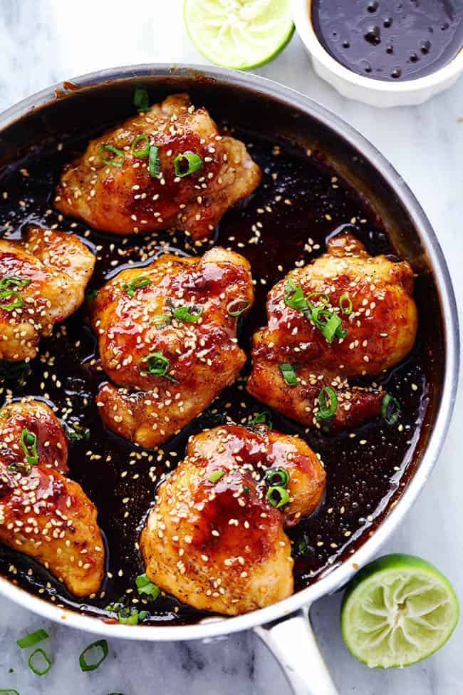 Asian glazed chicken cooking in a skillet garnished with onions and sesame seeds. 