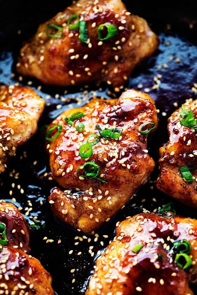 Sticky asian glazed chicken in a skillet garnished with scallions and sesame seeds. 