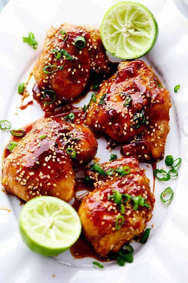 Sticky asian glazed chicken on a plate with a lime halved and garnished with scallions and sesame seeds.
