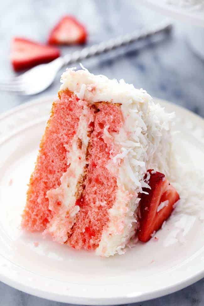 A slice of Strawberry Coconut Cream Cake with Coconut Cream Cheese Frosting on a white plate. 