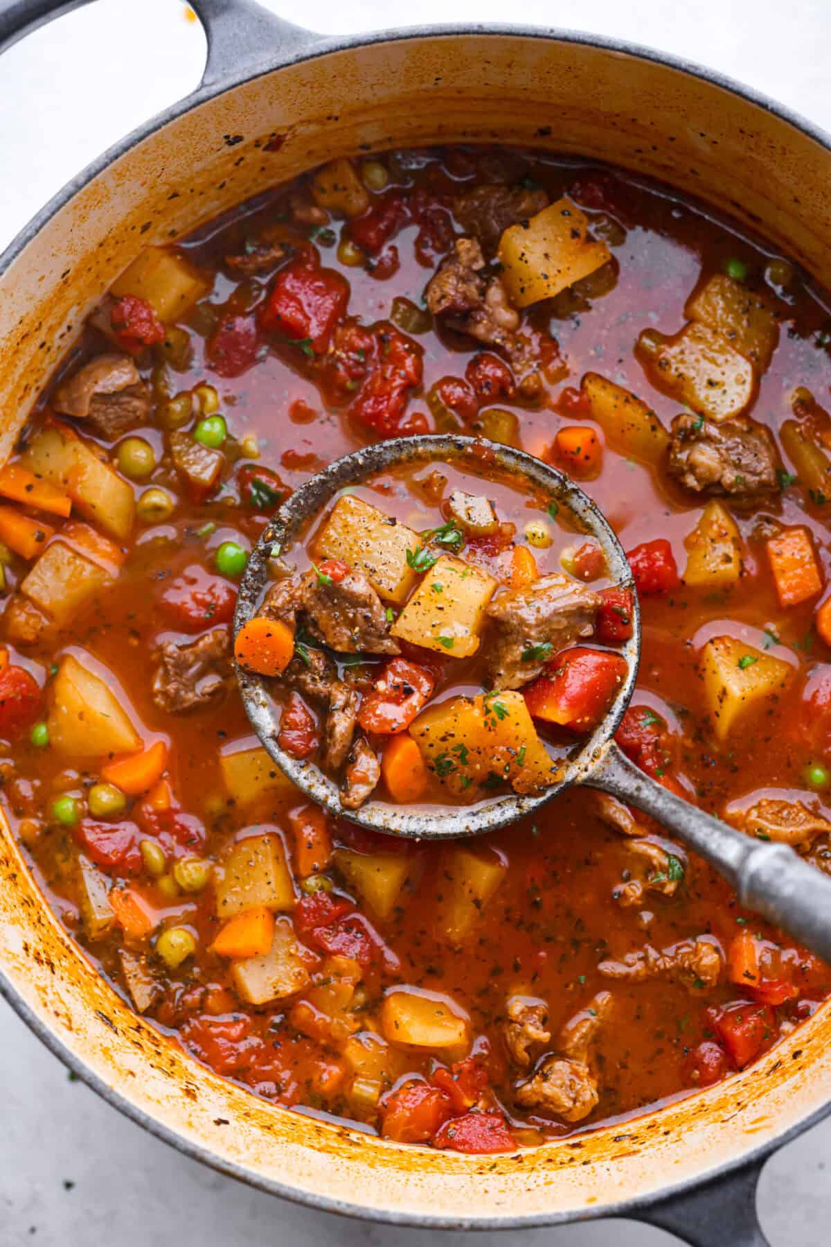 Top view of a ladle lifting vegetable beef soup in a large pot.