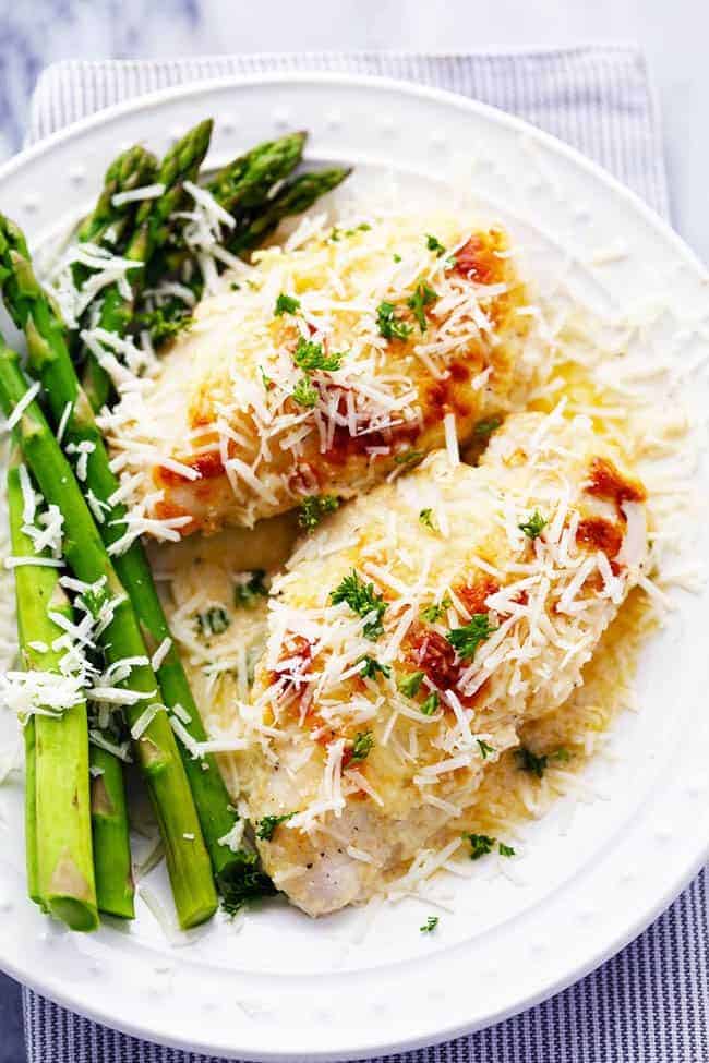 Creamy baked asiago chicken and baked asparagus on a white plate. 