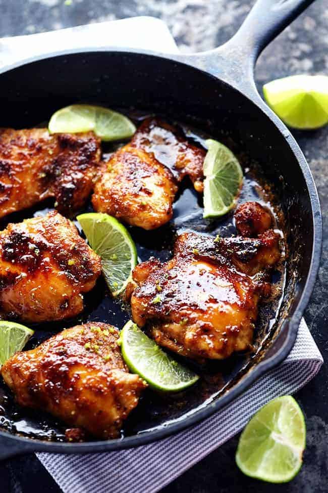 Skillet honey lime chicken in a large black skillet. There are freshly cut limes on the side of the skillet. 