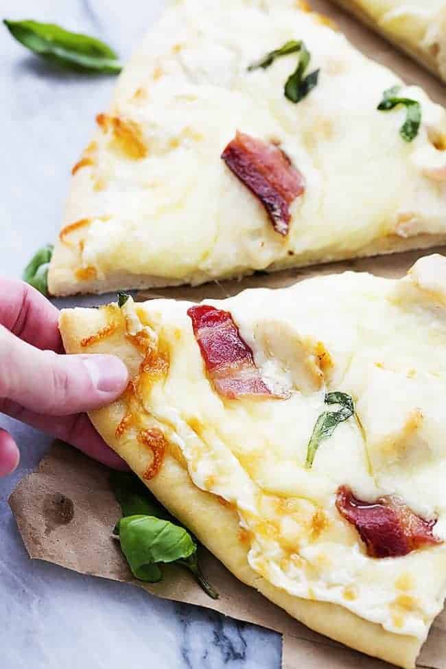 Bacon Chicken Alfredo Pizza that has been sliced with a hand taking a slice. 