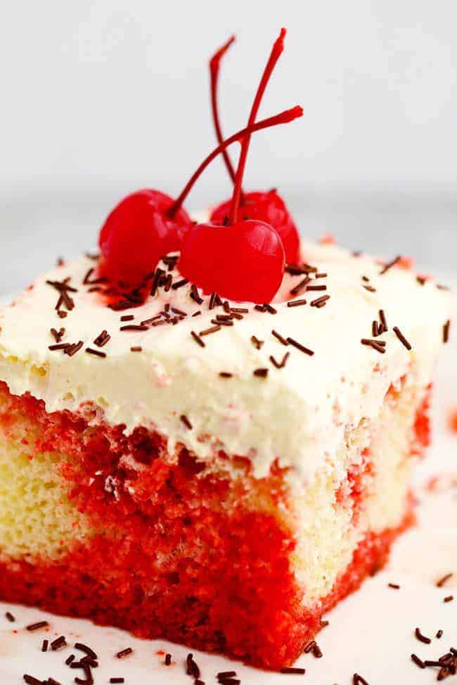 Close up photo of Cherry Jello Coke Poke Cake on a white plate with cherries on top. 