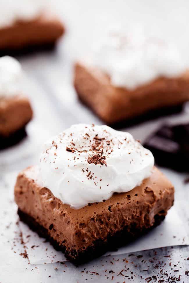 French Silk Pie Bars with whipped topping on parchment paper. 