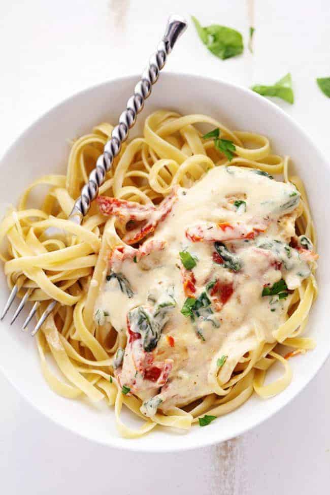 Creamy Tuscan Garlic Chicken over noodles in a white bowl with a metal spoon. 