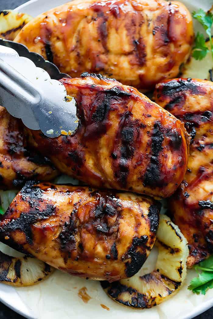 Grilled Hawaiian BBQ Chicken on a white plate with tongs removing one. 