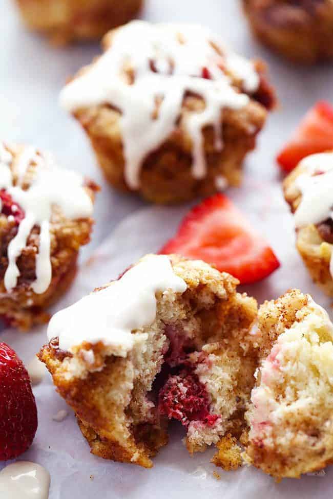 Strawberry Cinnamon Roll Muffins with a Cream Cheese Glaze. One of them is broken in half to show the inside. 